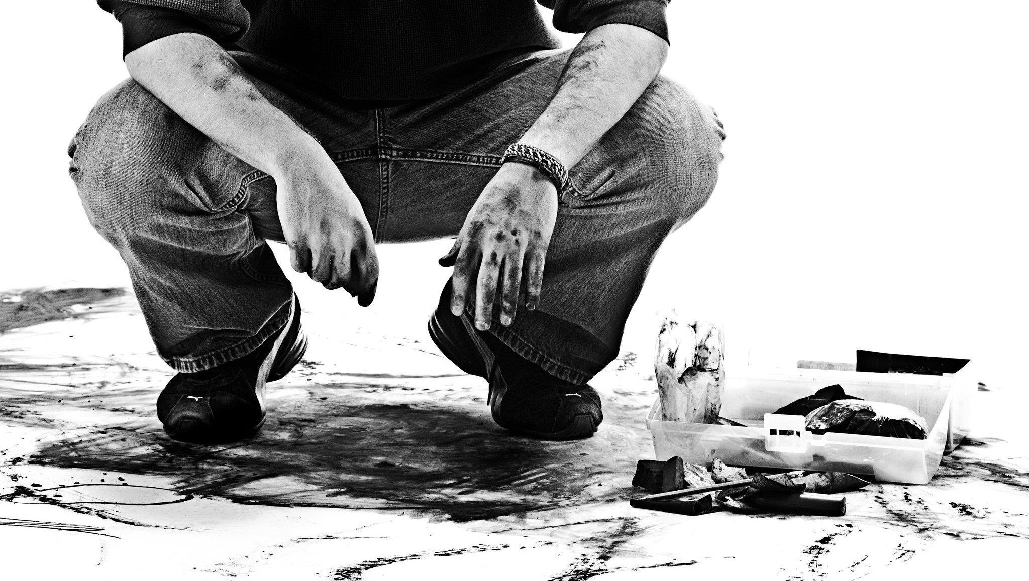 Samuel Gray crouched over a work in progress, charcoal on his hands
